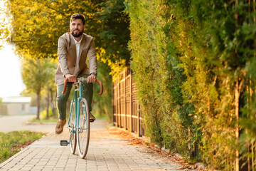 Young bearded businessman riding bicycle on city street