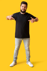 Fototapeta na wymiar Handsome man pointing at black t-shirt on yellow background