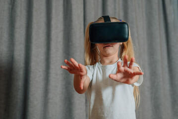 Obraz premium child girl at home in virtual reality VR glasses watching video, playing games. modern children are well versed in technological innovations. generation alpha