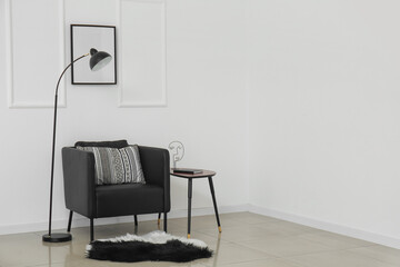 Black armchair, standing lamp and table near light wall
