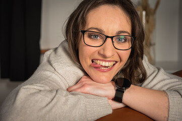 Success concept. Portrait of chic, young, emotional, pretty with glasses, sitting at work, leather brown chair in the office, smiling and showing tongue  