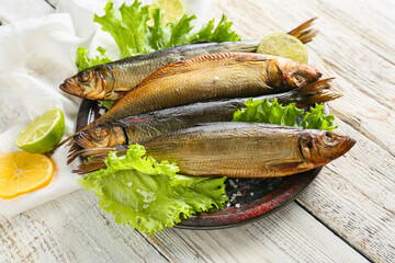 Plate with smoked herring fishes on white wooden background