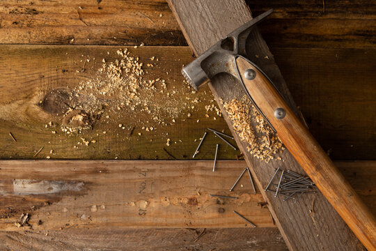 A hammer with nails sitting on a wooden board. 