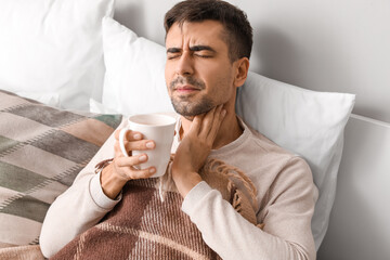Ill young man with sore throat drinking hot tea at home