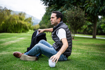 Caucasian Hispanic man working outdoors with laptop at park, sitting on grass. 