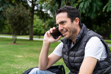 White Hispanic man using phone at park. Middle aged man talking by phone outdoors.