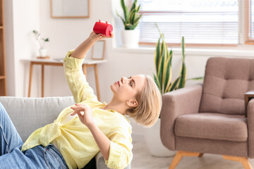 Woman with modern wireless portable speaker lying on sofa in room