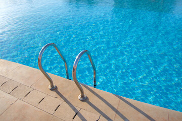 Close up of swimming pool stainless steel handrail descending into tortoise clear pool water. Accessibility of recreational activities concept