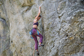 Determined girl climber clambering up steep wall of rocky mountain. Sportswoman overcoming difficult route. Engaging in extreme sports and rock climbing hobby concept