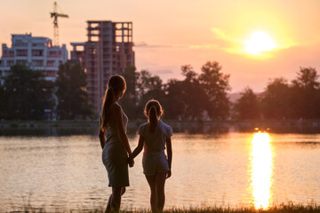 Happy mother and daughter standing together looking at building under construction dreaming about their future home at sunset. Family love and relationship concept
