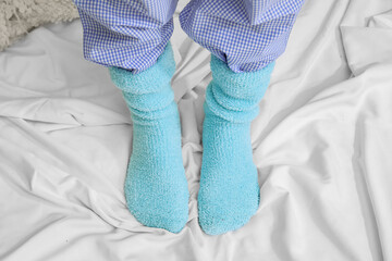Woman in warm knitted socks on bed, closeup. Concept of heating season