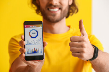 Sporty man holding phone with installed app for calories counting and showing thumb-up on color...