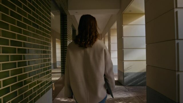 Camera follows young woman, student or manager employee walk through alleyway in university campus or business district, hold laptop in her hand. Concept study abroad or millennial workforce