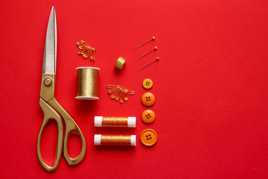 Thread spools, scissors, buttons and pins on red background