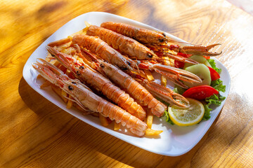 Fried langoustines with french fries and lemon on the table at sunny day
