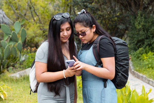Mujeres jóvenes con cabello largo sorprendidas por algo en el móvil abrazándose en una parque,espacio libre,
