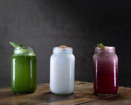 Limonada de yerbabuena, limonada de coco y limonada de frutos del bosque sobre una mesa de madera con un fondo gris