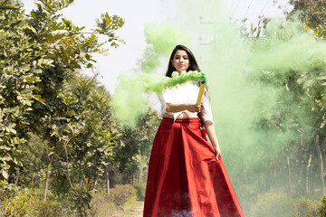 Fototapeta premium Beautiful young girl woman celebrate festival of color holi with Multicolored smoke bombs dry color Holi powder colour gulal abeer in the park in spring break festival of color