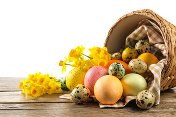 Overturned basket with painted Easter eggs and flowers on table against white background