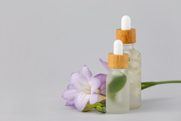 Bottles of natural cosmetic product with herbal extract and flowers on grey background