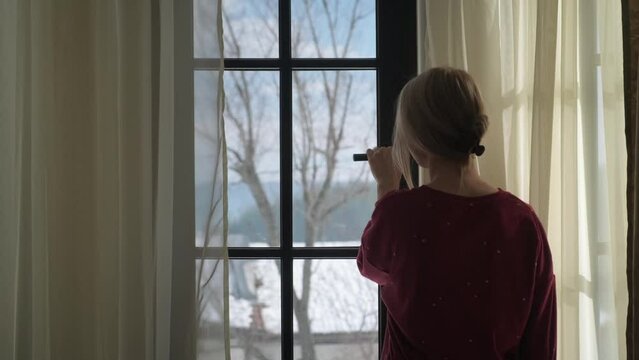 Young woman opening window at winter chalet at the morning and stretching.
