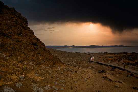 A long trail by the side of the mountain leads to the sea under a gray sky in the sunset