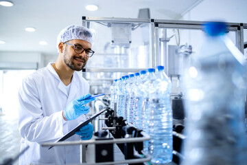 Technologist working in bottling factory doing quality control of drinking water before...