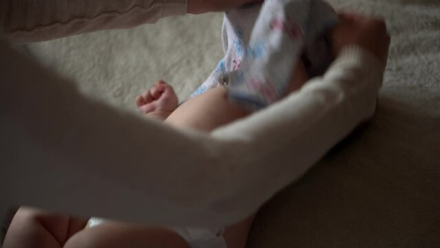 Newborn Baby And Young Mom Lie On Bed. Cute Smiling Teethless Kid Face Portrait. Woman With Child Put Off Bodysuit. Mother Care Of Babe. Infant, Mother Day, Childbirth, Beginning, Relationship Concept