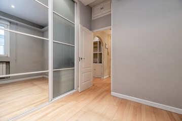 Dressing room with large built-in wardrobe with glass and mirror doors, wooden floors and white woodwork.