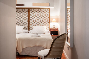 Bedroom with metallic gold headboard, upholstered armchair and wooden floors with towels on the bed