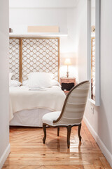 Bedroom with metallic gold headboard, upholstered armchair and wooden floors with towels on the bed
