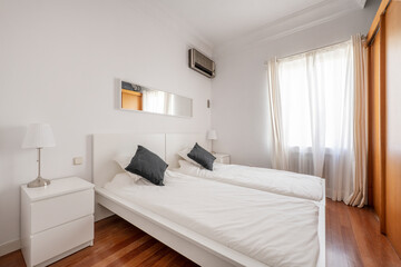 Fototapeta na wymiar Bedroom with two single beds, mirrored headboard and white wooden tables and cherry parquet floor