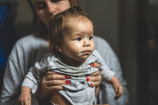 unknown mother holding her baby nasty small caucasian child little girl with food around her mouth and on dirty face making mess at home childhood and growing up concept copy space growing up