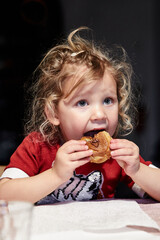 petite fille de trois ans mange un chou à la crème au chocolat à pleine dents