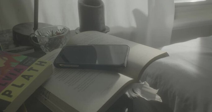 Close up of an iphone ringing on top of an open book which then closes, surrounded by bedroom decor, poetry, and feminist books