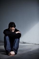 Dealing with emotional stress. A young man looking worried while sitting barefoot on the ground.