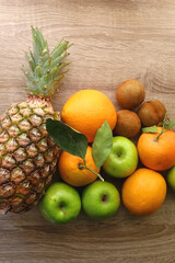 Pineapple, apples, oranges, lemons and kiwis on a wooden table. Top view.