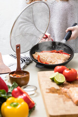 grilled chicken with seasoning in frying pan covered in splatter screen on modern kitchen counter