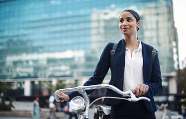 Welcome to the city, where opportunity awaits. Shot of a young businesswoman traveling with a bicycle through the city.