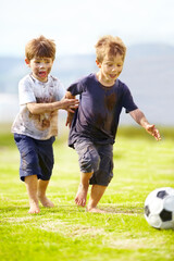 Having a friendly game. Two cute little boys playing soccer together outside while covered in mud.