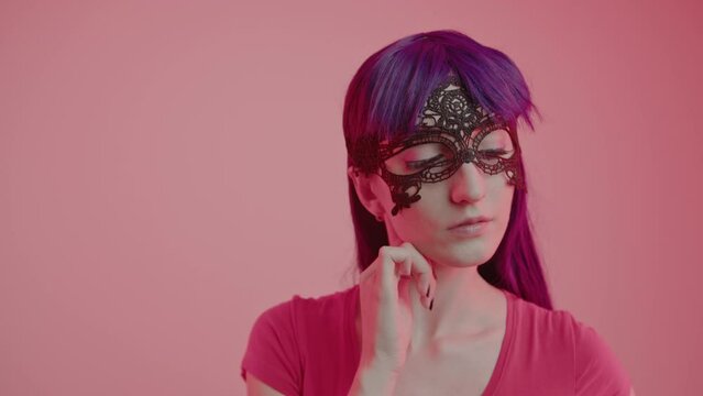 Enigmatic European Woman Wearing a Silk Mask Looks Attractively into the camera medium close-up shot pink background. High quality 4k footage