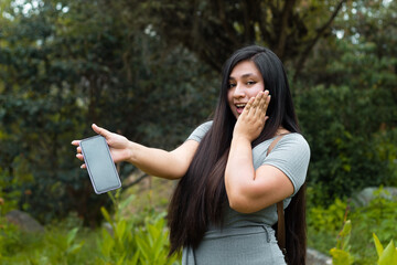 Una mujer latina emocionada  con un teléfono inteligente y lee buenas noticias, se siente feliz,...