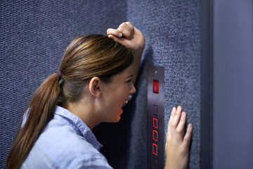 Im stuck in here. Shot of a fearful woman shouting into an elevator intercom. - obrazy, fototapety, plakaty