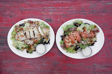 Cesar salads. Top view of two Cesar salads with lettuce, parmesan cheese, bread croutons,  bacon and Caesar dressing. One with grilled chicken breast and the other one with smoked salmon.