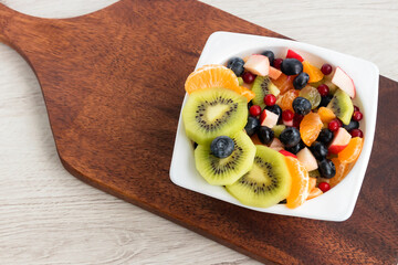 Freshly prepared fruit vitamin healthy salad of kiwi, tangerine, apple, cranberries, blueberries, grapes in a white bowl on a kitchen board.Isolated on a white background.