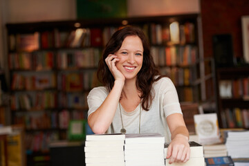 Ive worked hard to make my bookstore successful. Portrait of a young woman leaning on stacks of books in a bookstore.