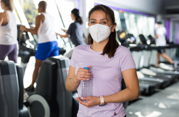 Portrait of girl in protective mask with bottle of water in a sports club