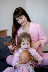 Mother combs her little daughter's hair while sitting in bed in morning. Good morning.