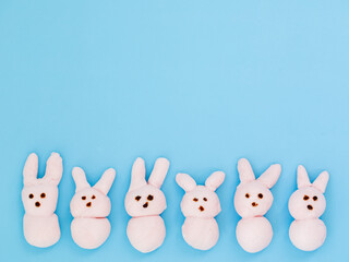 Obraz na płótnie Canvas Pink handmade marshmallow candy bunnies on blue paper background with copy space for your Easter text message. Minimal happy Easter holiday conceprt. Top view flat lay, border frame.