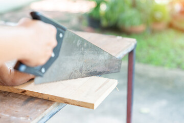 The carpenter use hand saw to cut wood sheet for build furniter.